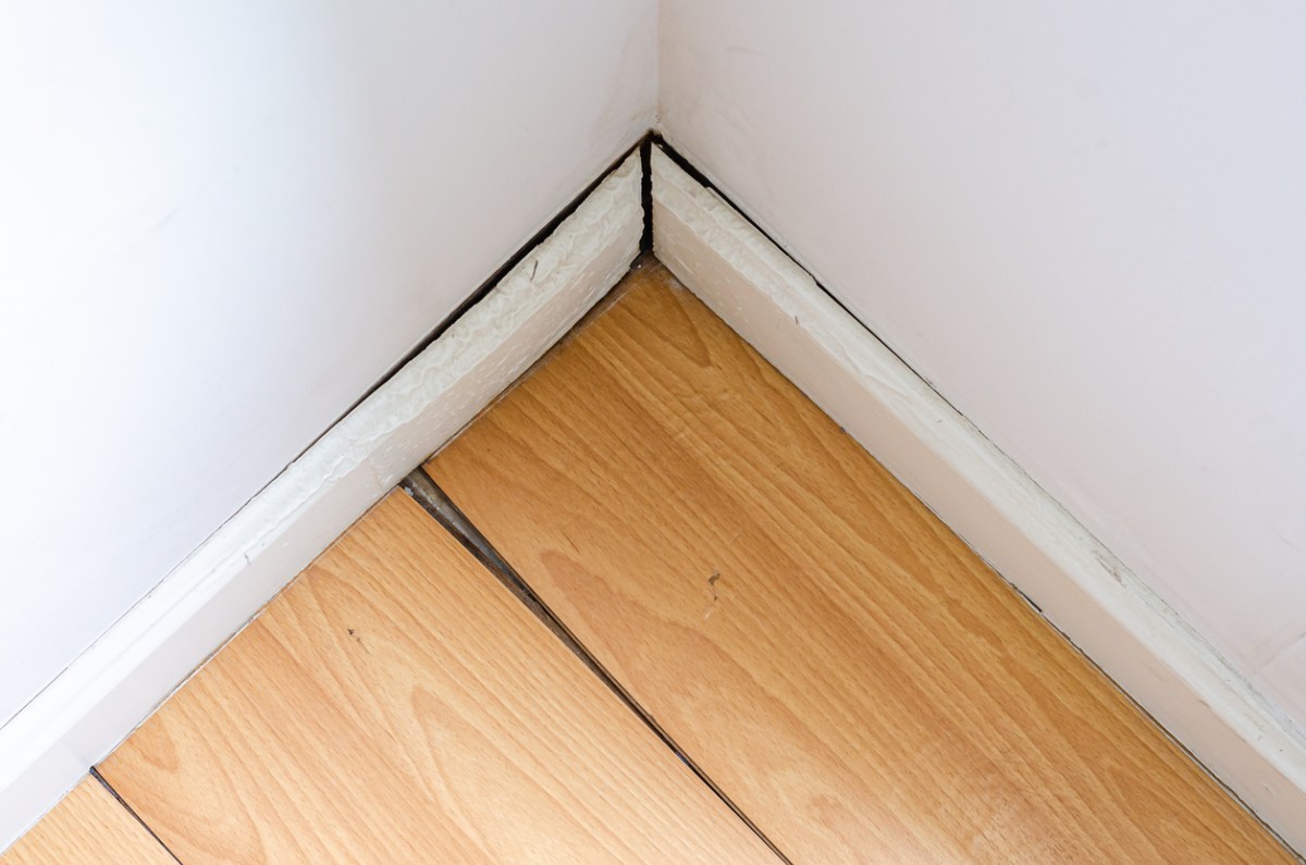 Poorly installed white baseboards next to wooden floors.