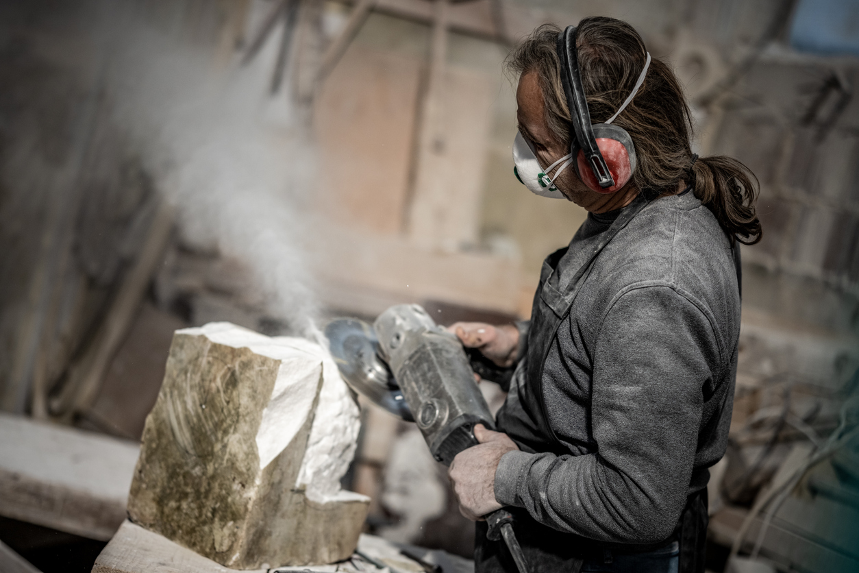 A-person-uses-a-hand-saw-to-cut-a-block-of-stone-while-wearing-a-mask.