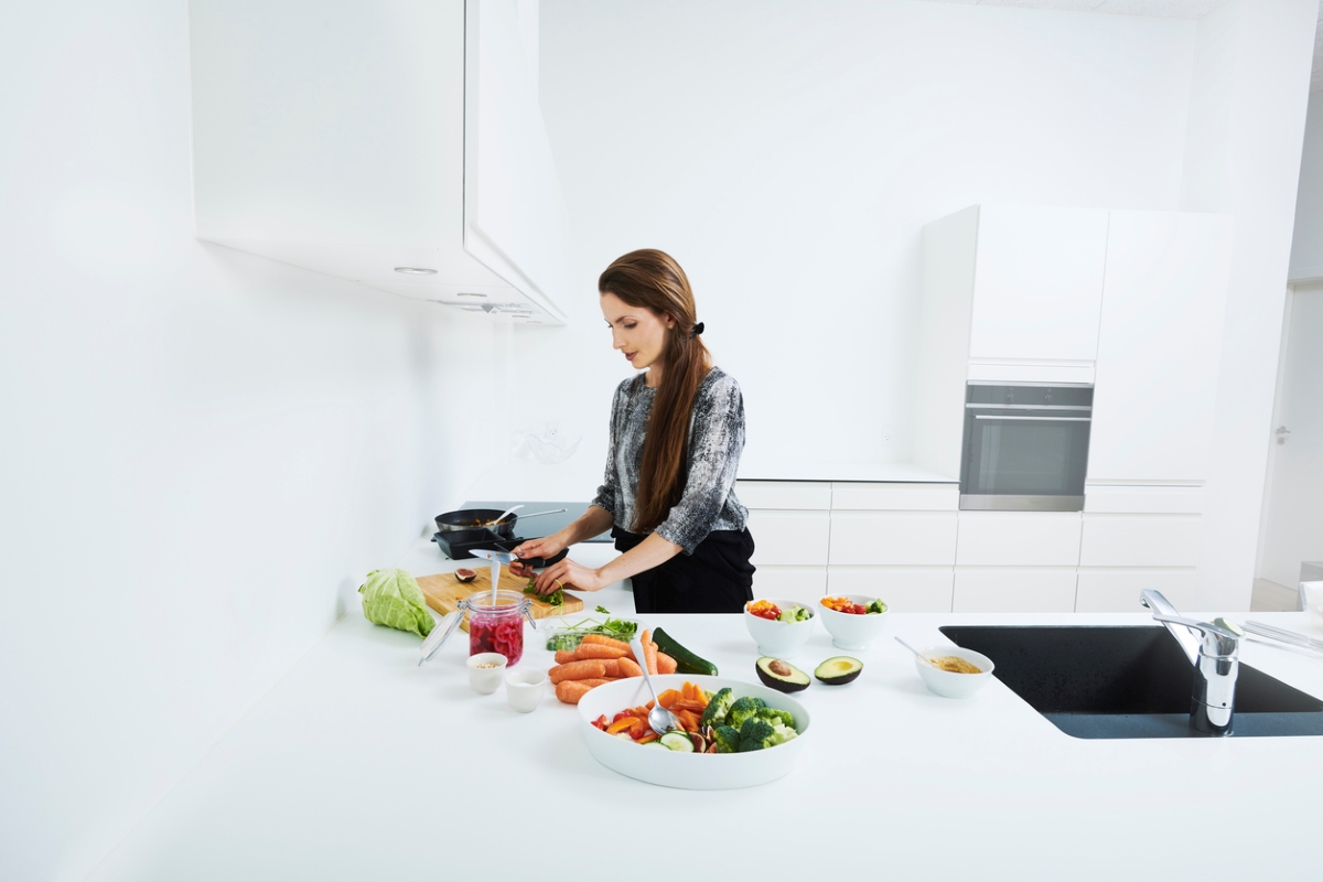 Woman cooking with colorful ingredients in white kitchen.
