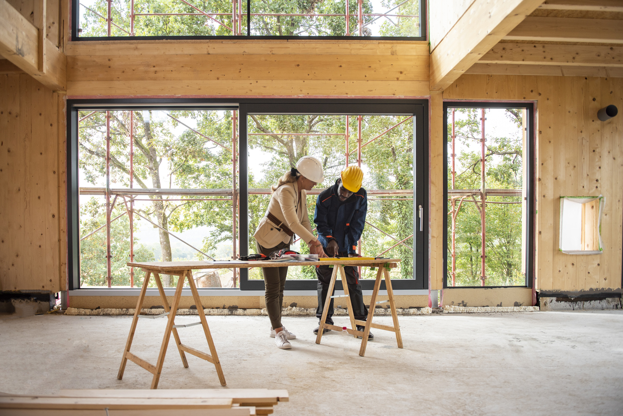 Man and woman contractors wearing hard hats in new home build while going over plans.