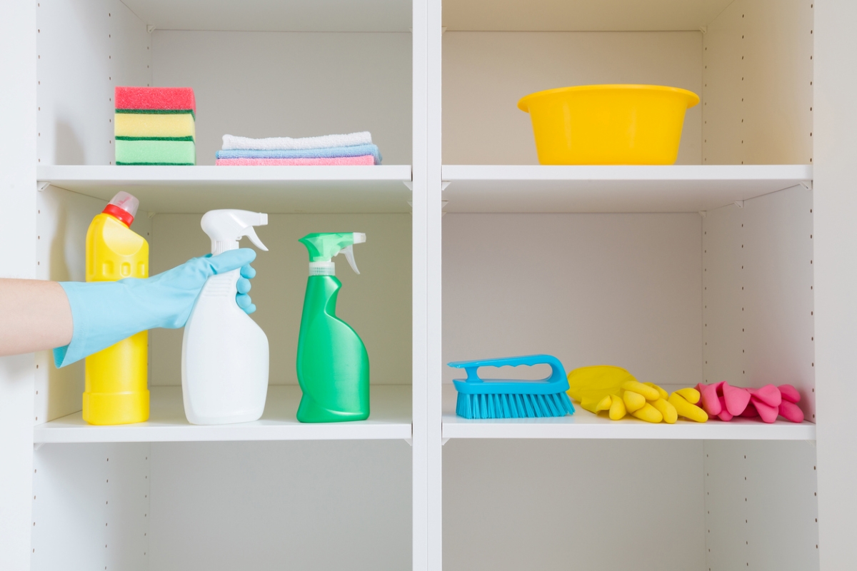 Person putting spray bottle with other cleaning supplies in supply closet.
