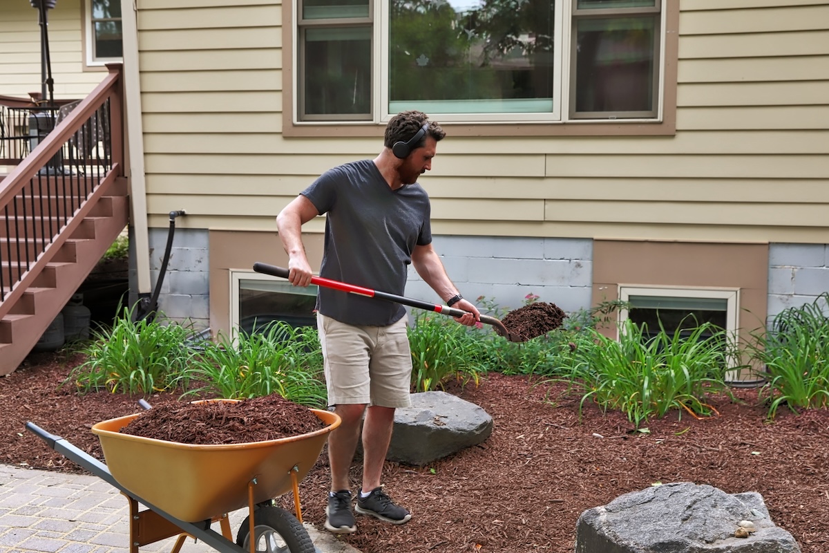 A homeowner laying down wood mulch in his backyard flower beds.