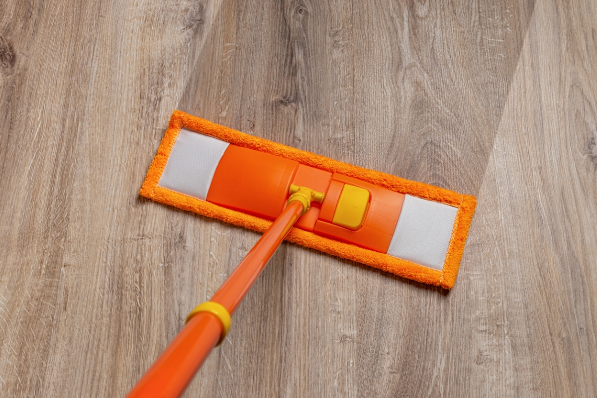 Orange mop cleaning vinyl wood flooring.