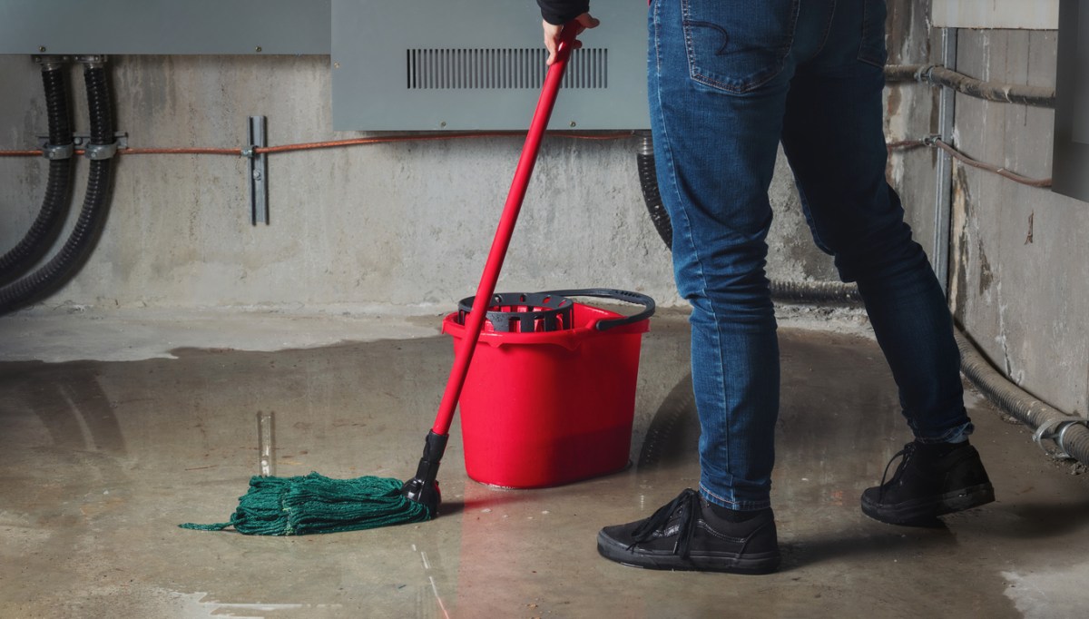 Man cleans up basement flooding with red bucket and mop.