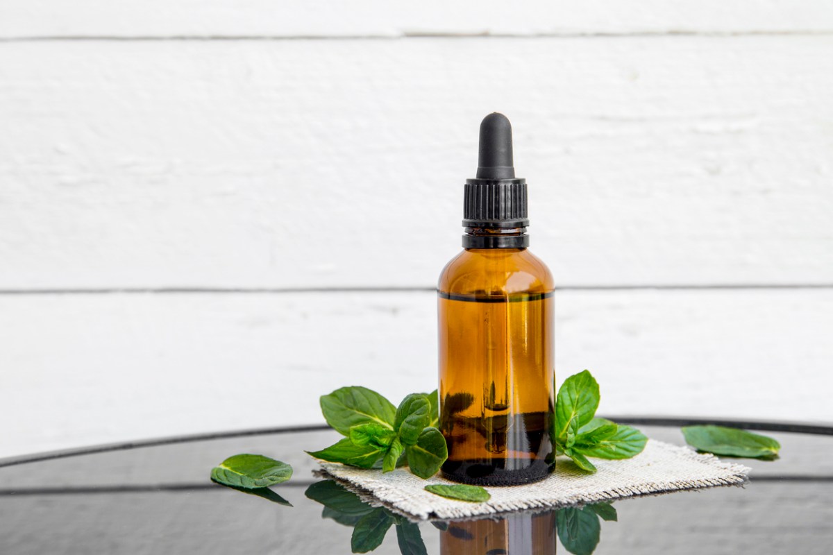 A brown bottle of peppermint essential oil surrounded by mint leaves.