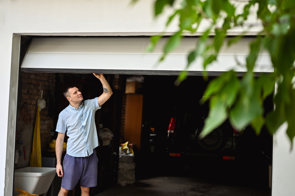 Young man with white shirt and blue shorts walks through attached car garage.