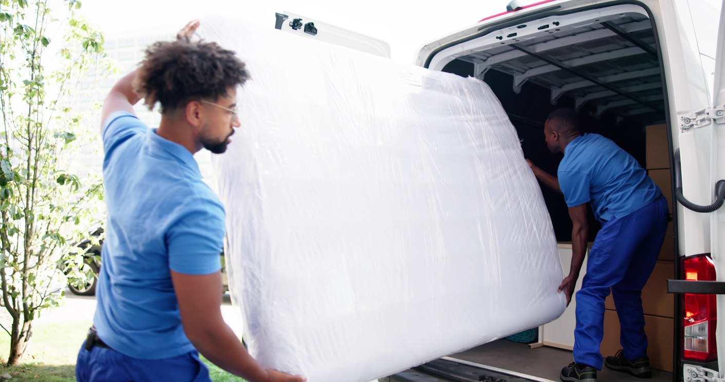 Two-men-load-a-mattress-into-the-back-of-a-van.