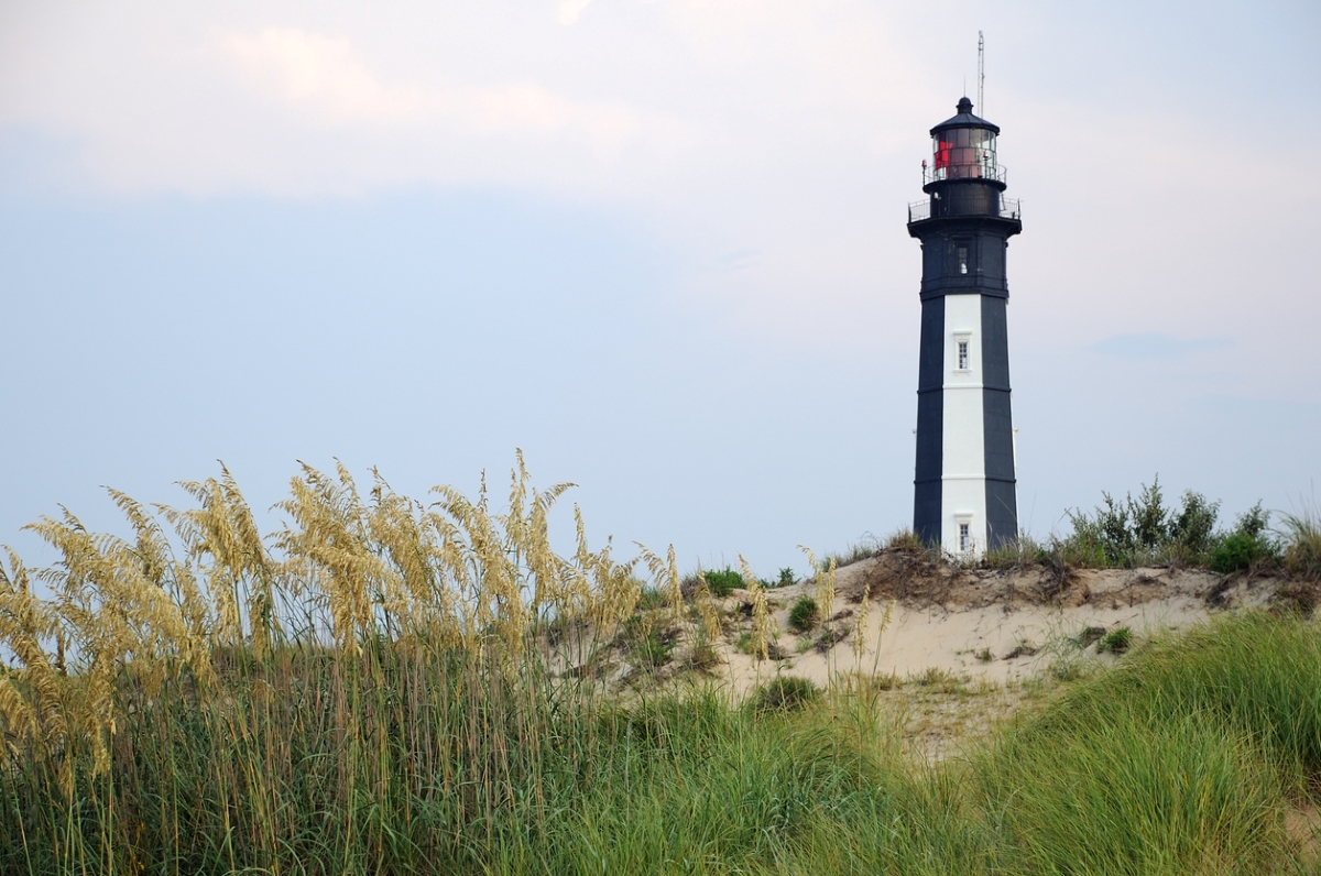 Lighthouse on grassy beach landscape.
