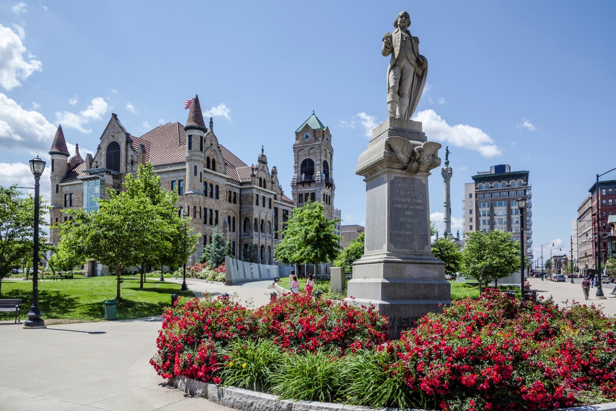 Historic figure statue in front of large courthouse with flowers.