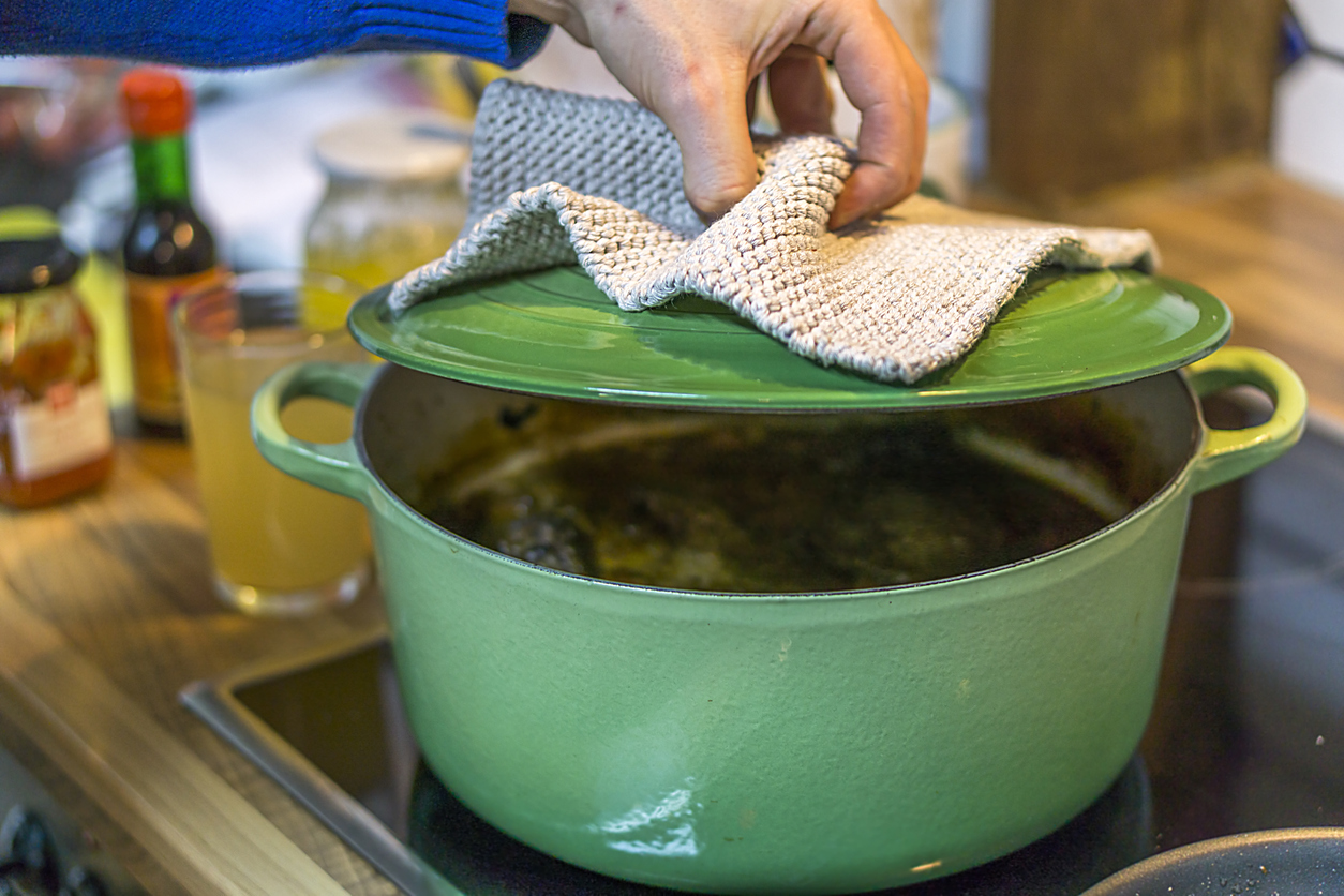 Green enamel pot on cooktop with steam escaping.