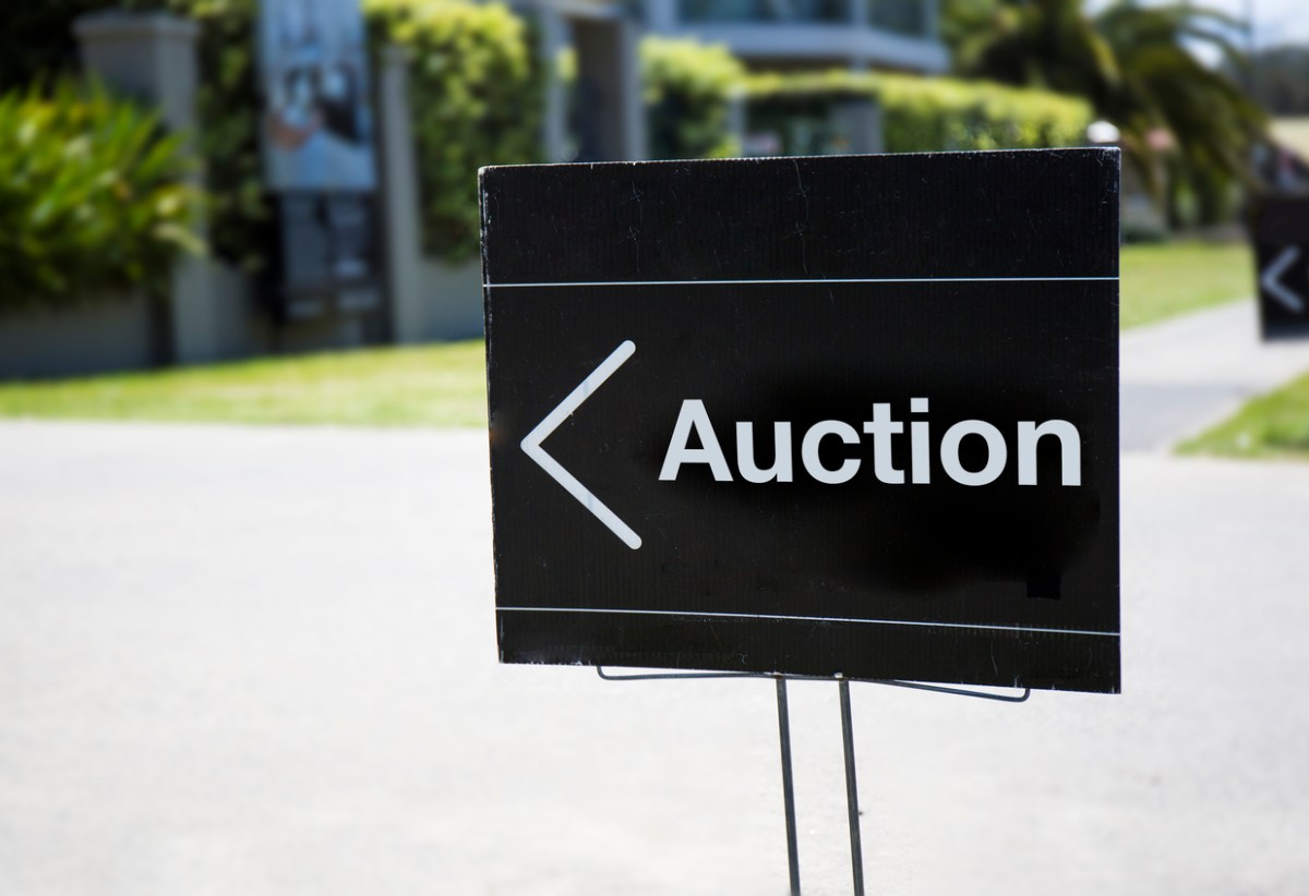 A-black-and-white-sign-with-the-word-Auction-sits-along-a-street-in-a-treed-neighborhood.