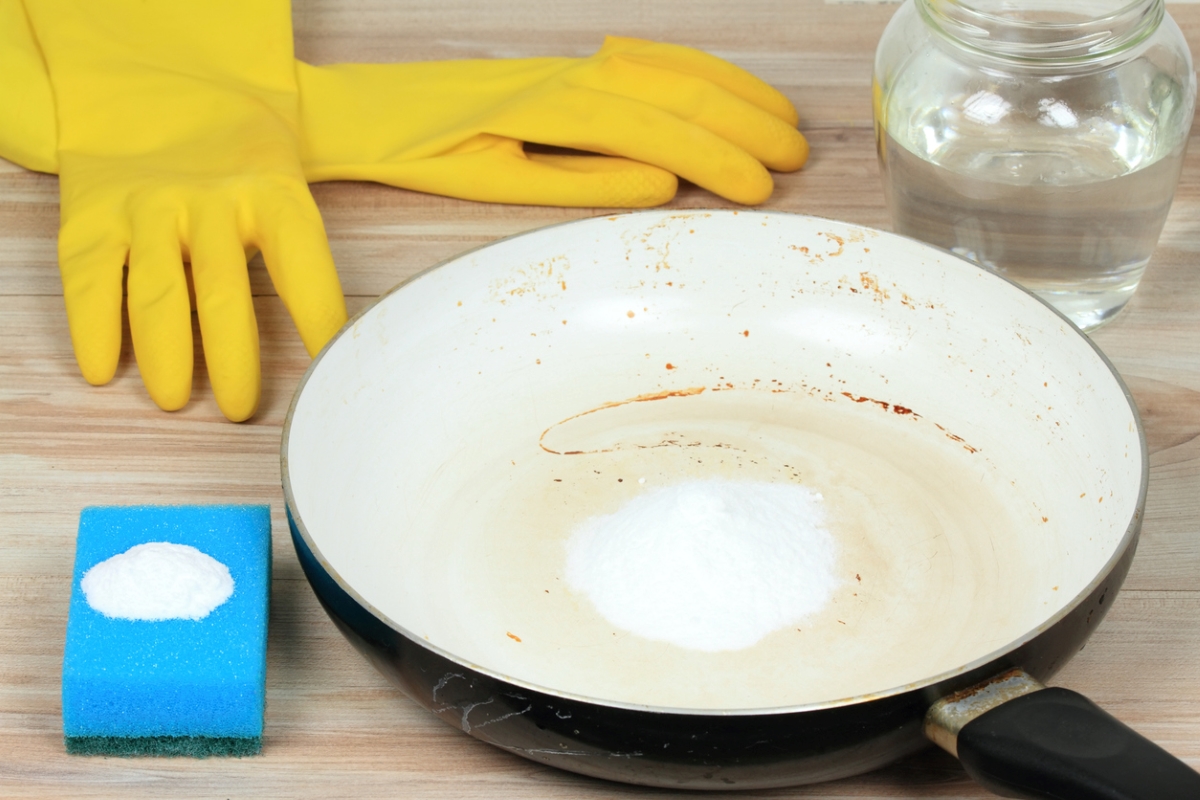 Burnt pan with baking soda next to glass of vinegar and gloves.