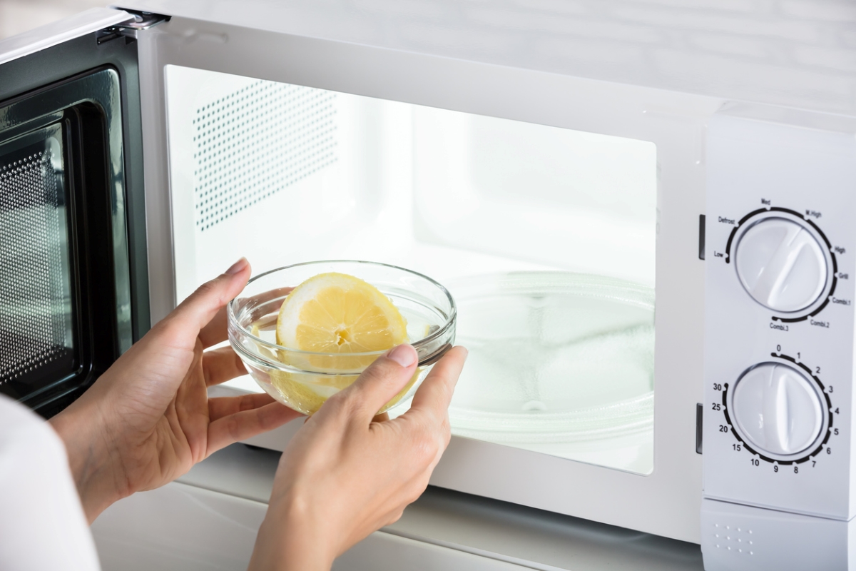 Person putting bowl with lemon in microwave.