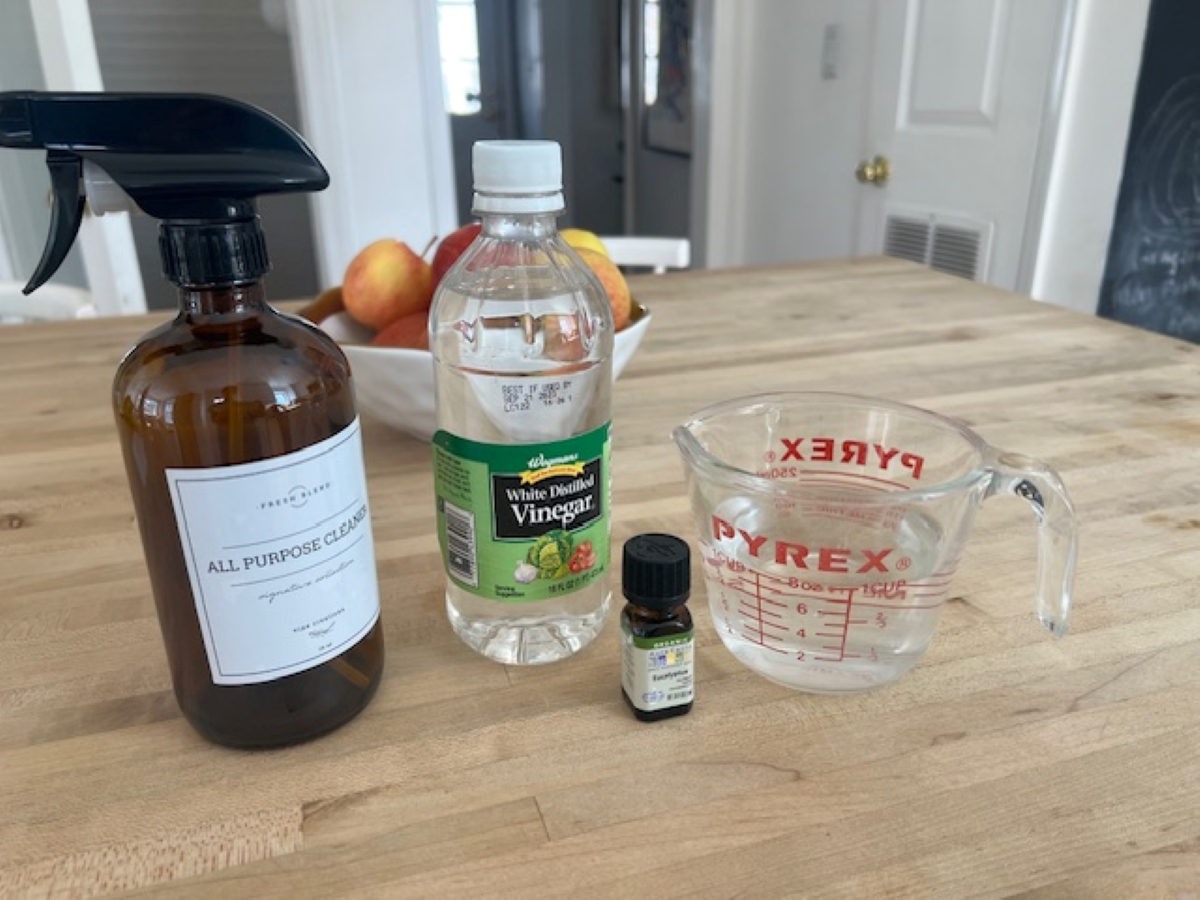 Bottle of vinegar next to measuring cup and spray bottle.