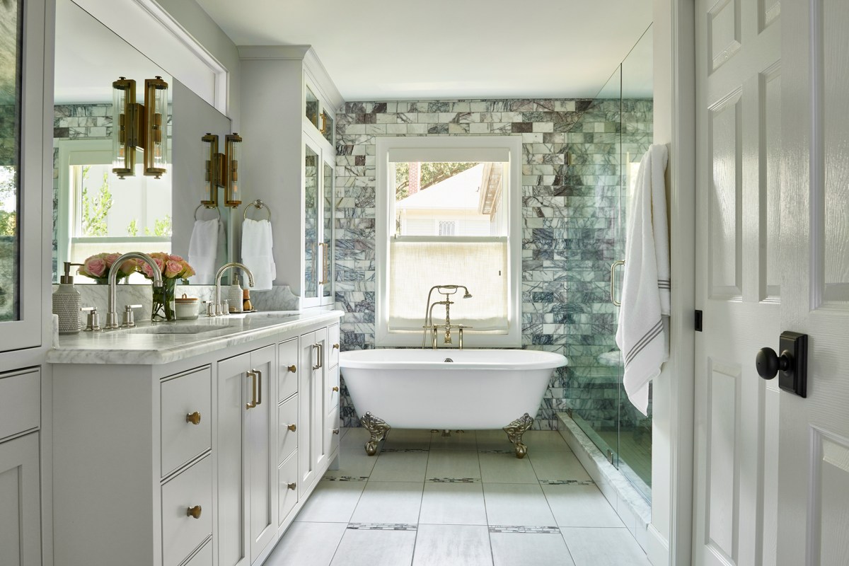 A bathroom has a freestanding tub and a wall of handmade tiles.