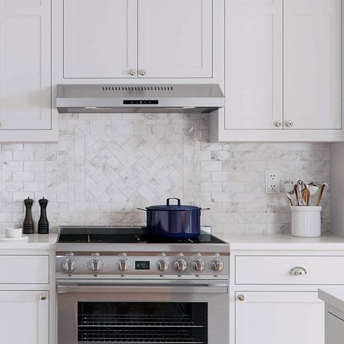 A built-in cabinet range hood in a white kitchen with a blue pot on the stove.