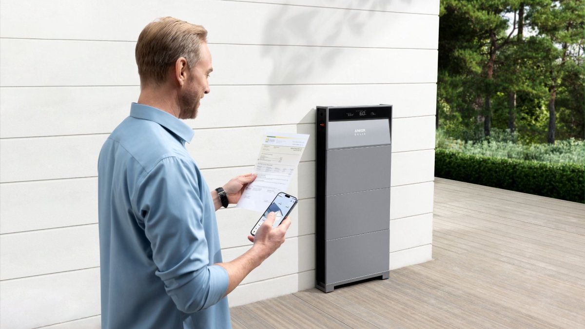 Man reading through utility bill outside of a house next to Anker's Solix X1 energy storage system