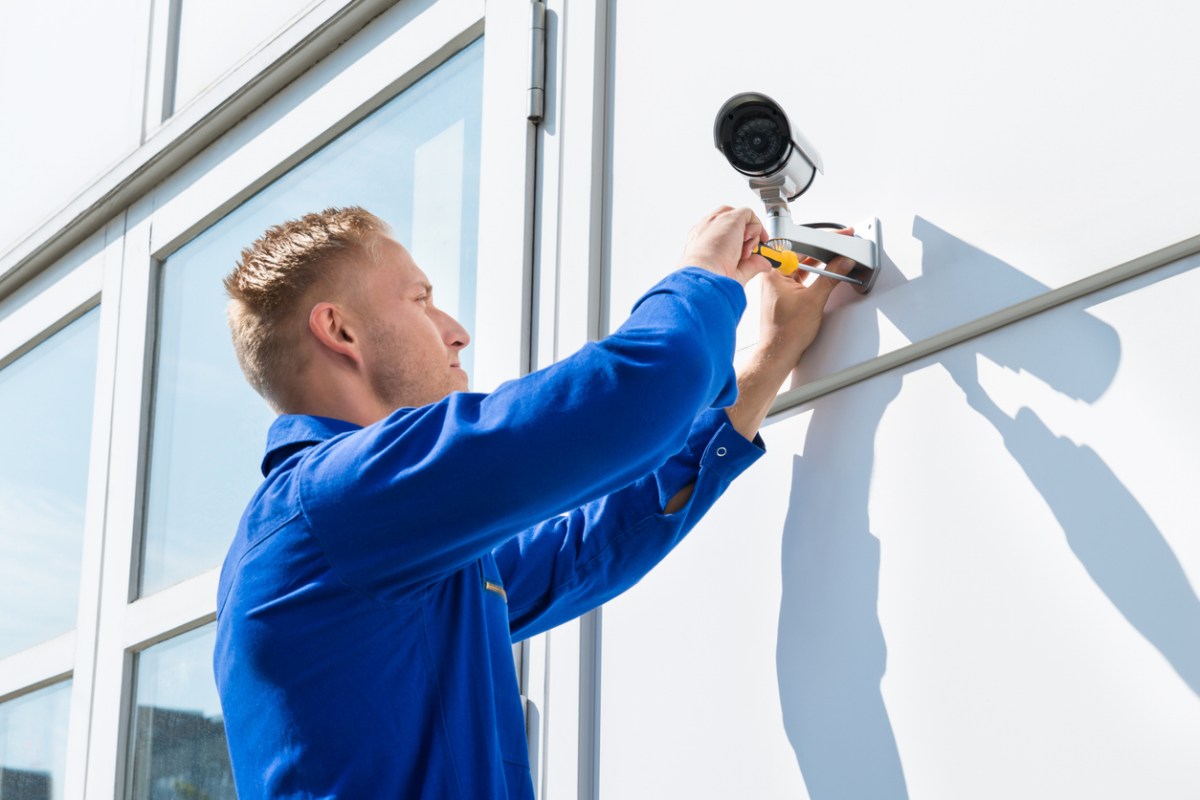 A close up of a worker installing a security camera on a home's exterior. 