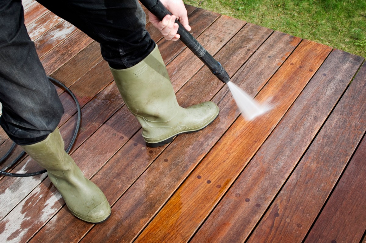 A close up of a person in green boots pressure washing a deck.