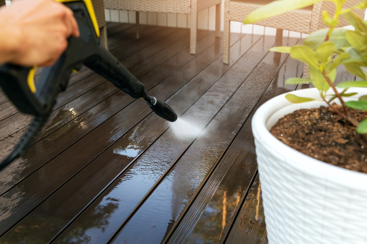 A close up of a person pressure washing a deck. 