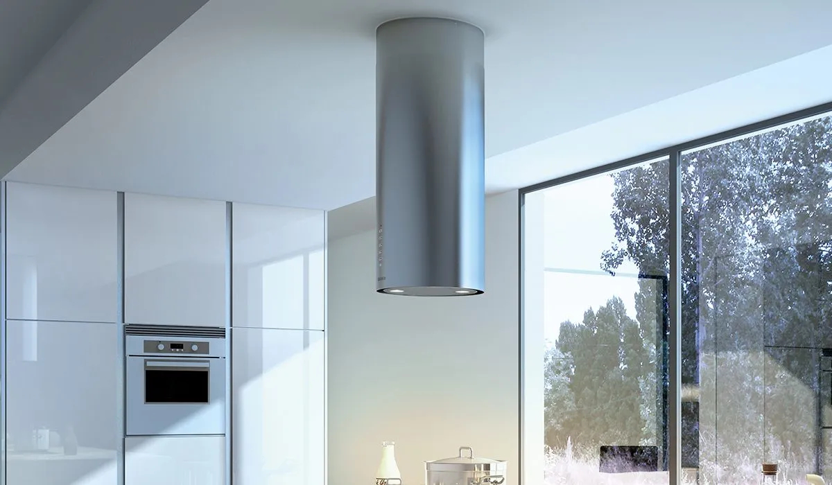 A cylindrical stainless steel oven range hood in a white kitchen with a large window.