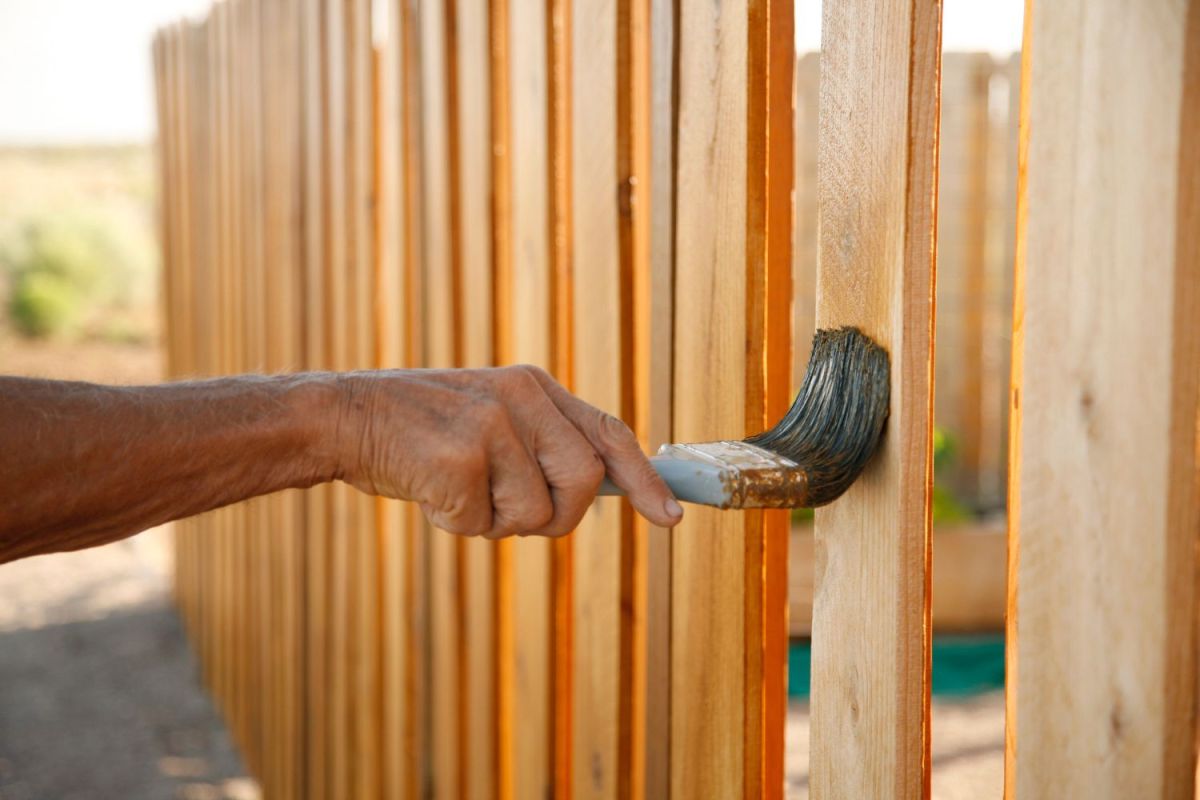 A close up of a hand painting a wooden fence.