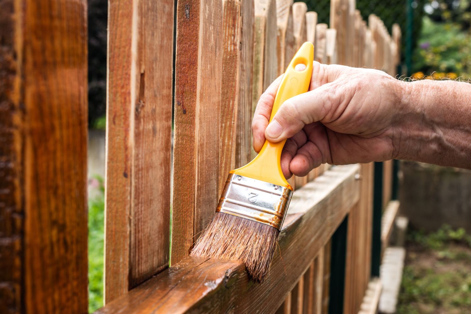 A close up of a hand painting a fence. 