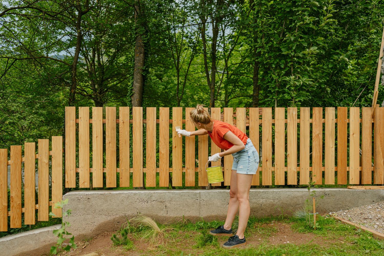 A woman paints a wooden fence. 