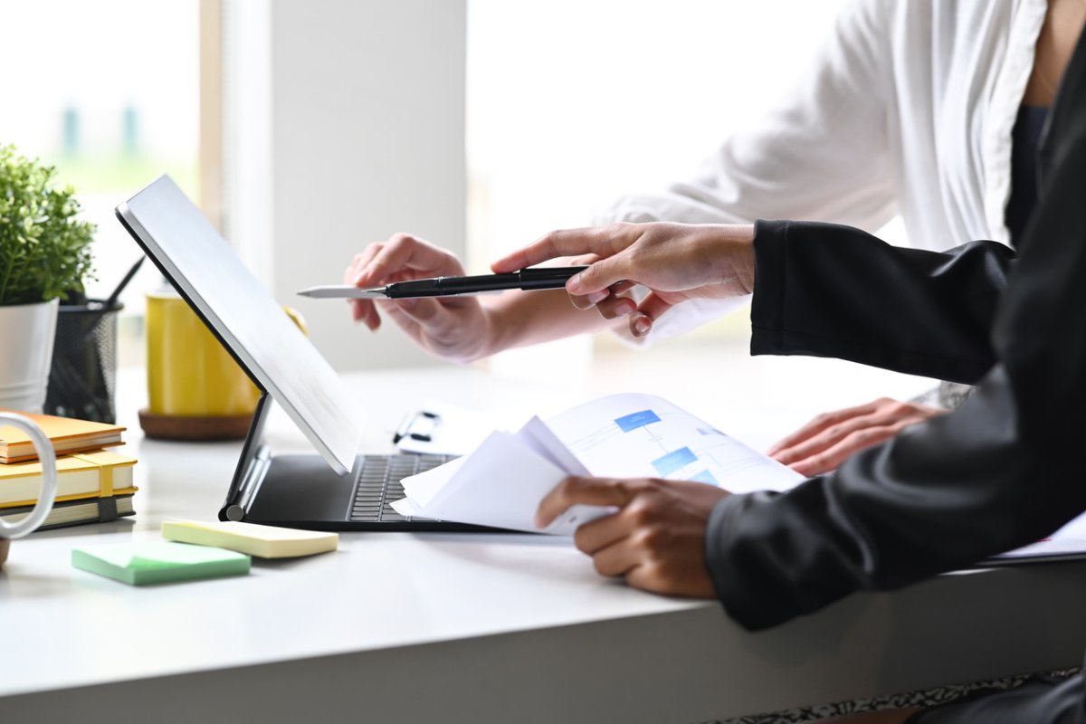Two people discuss a project together while looking at documents and a computer.