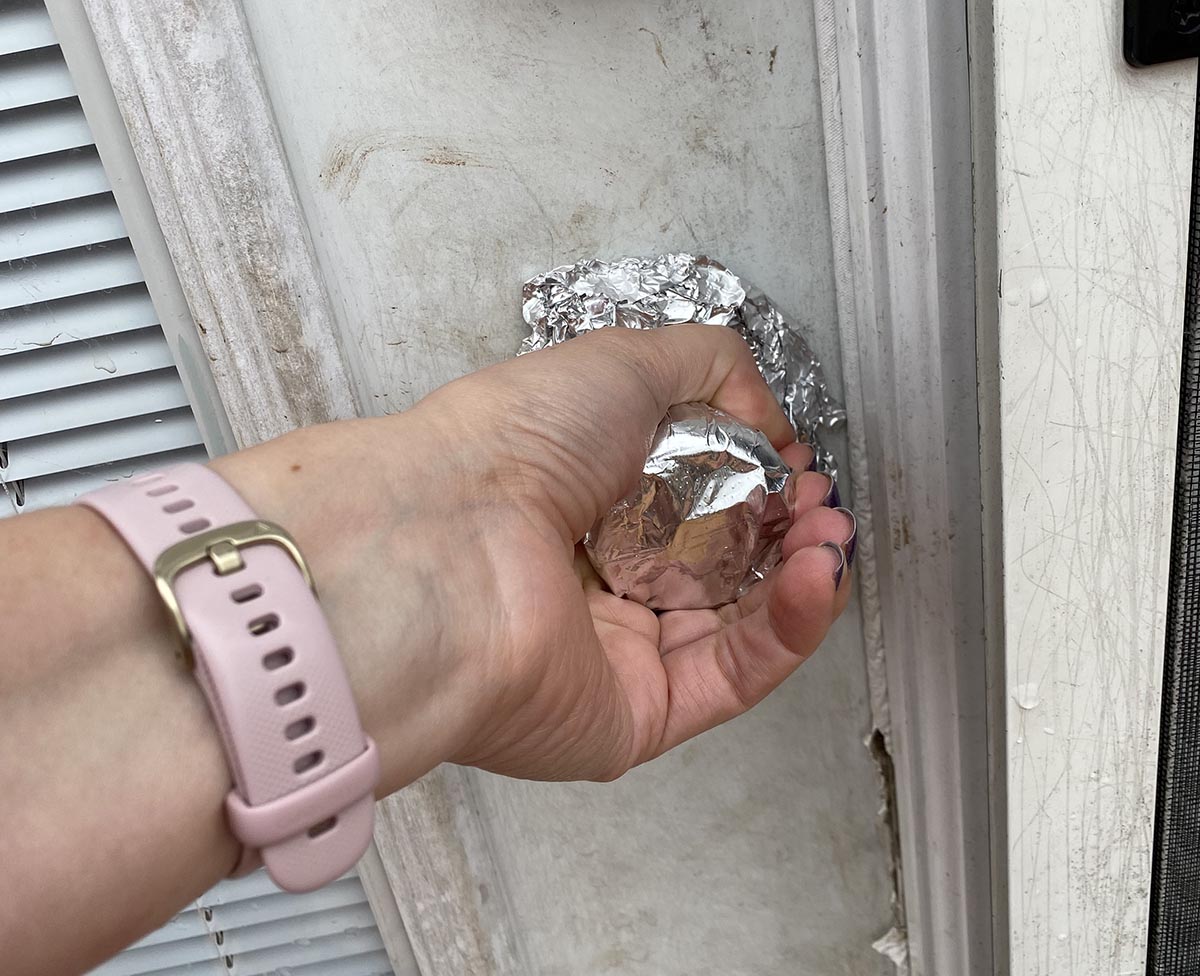 A hand grabs a door knob covered in aluminium foil.