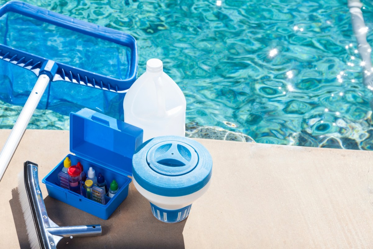 A close up of pool cleaning supplies in front of a pool.