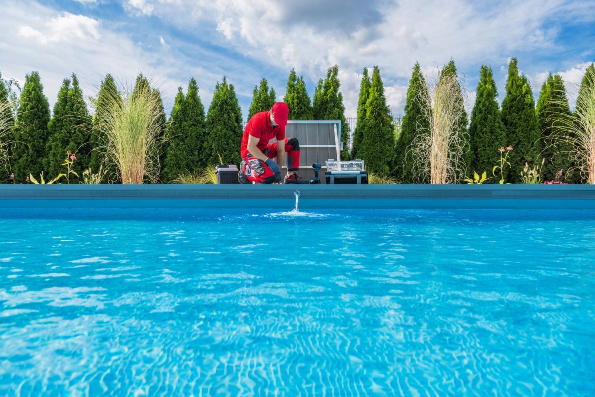 A worker cleans a pool on a bright and sunny day.