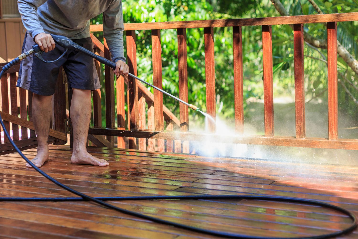 A close up of a person pressure washing a deck on a sunny day.