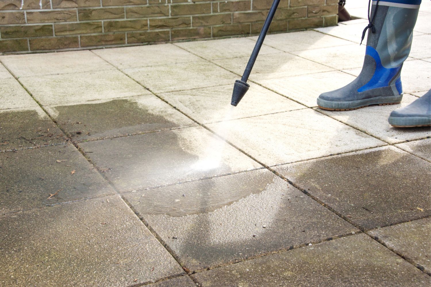 A close up of a person pressure washing a patio.