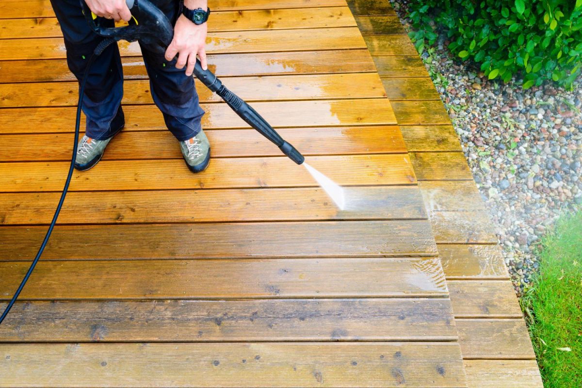 A close up of a person pressure washing a deck.