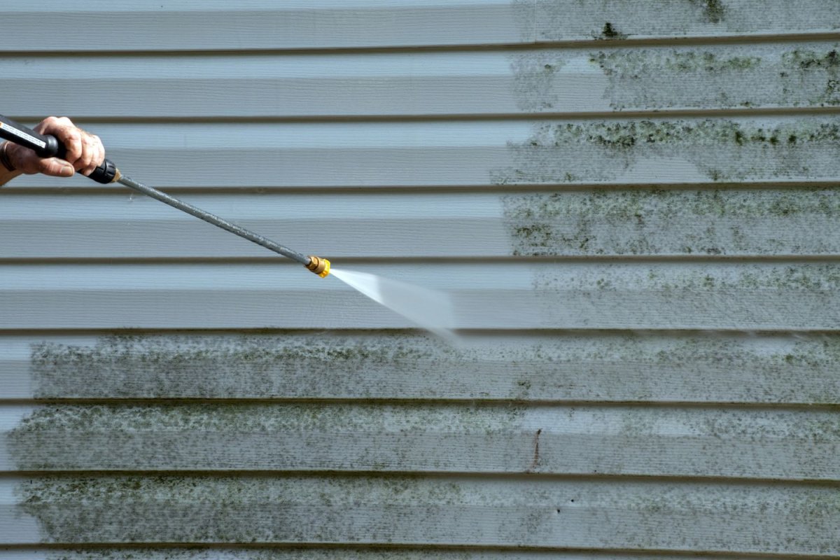 A close up of a pressure washer cleaning the siding of a house.