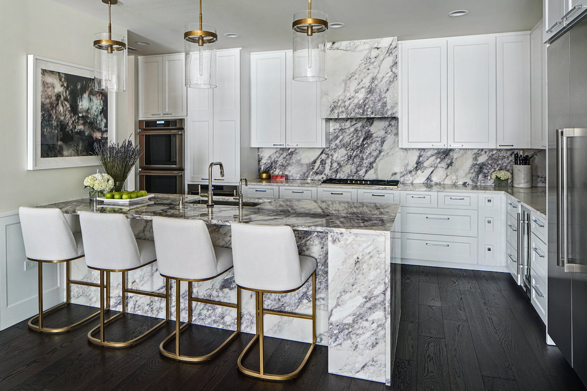 A marble range hood in a marble, white, and gold themed kitchen.
