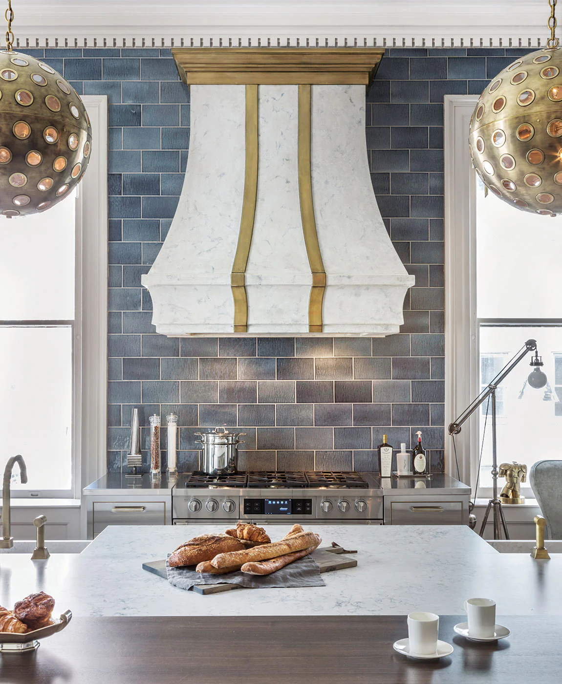A marble and gold range hood in a kitchen with blue tiled backsplash.