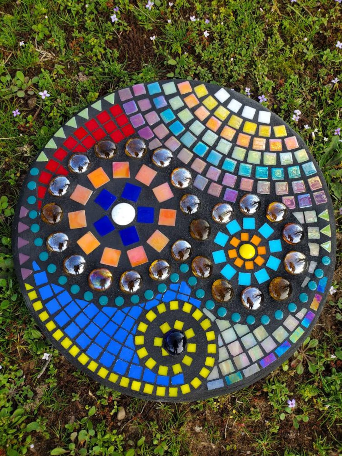 A round garden stepping stone with a colorful mosaic flower pattern.