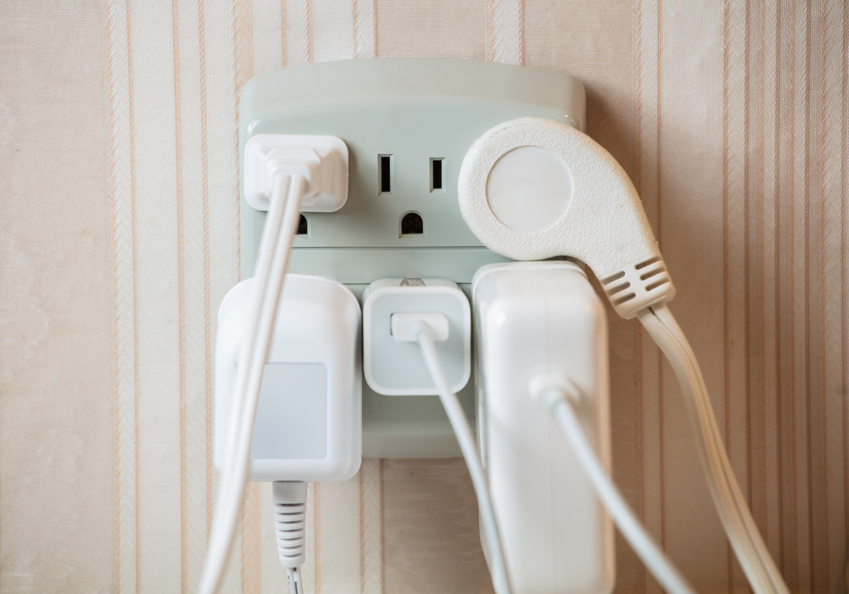 A multi-outlet power strip with various power cords and wall chargers plugged into it, likely too many for the wall outlet it is plugged into itself.