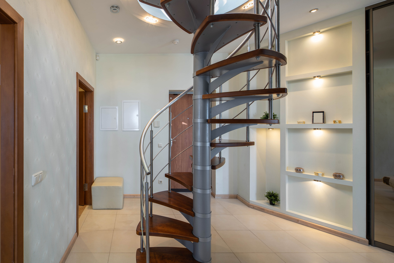 A narrow spiral staircase with walnut steps and a metal banister.