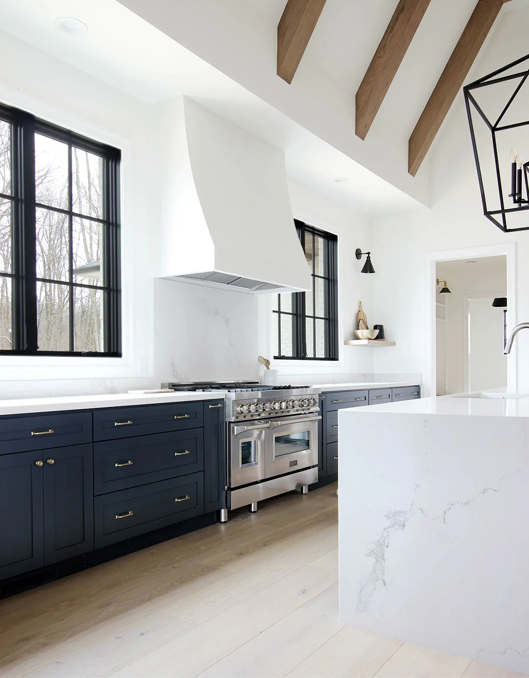 An oven range hood surrounded in plaster in a white marble and navy themed kitchen.