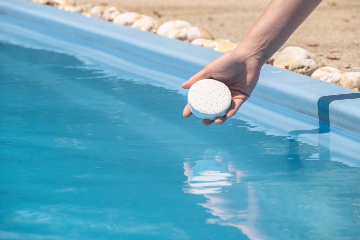 A close up of a person putting a chemical in a pool.