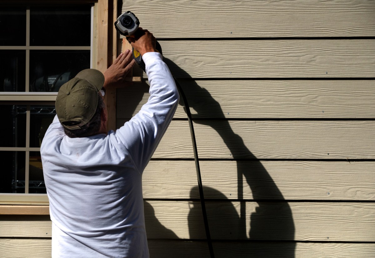 A worker uses a nail gun to install siding on a home.