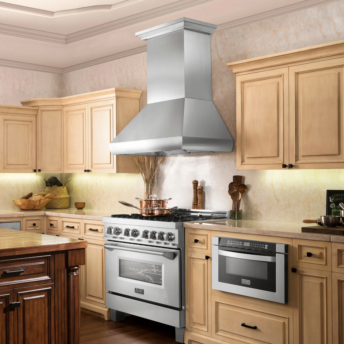 A stainless steel range hood in a kitchen with light-colored wood cabinets.