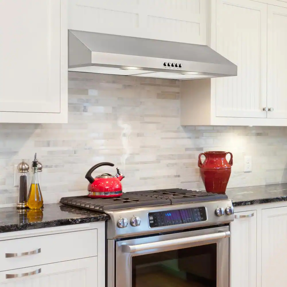 A stainless steel range hood under a cabinet in a white kitchen.