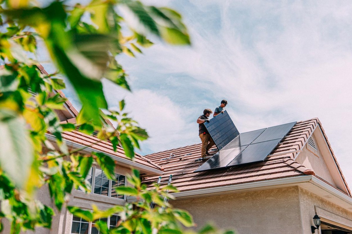 A view of two workers installing solar panels on a roof. 