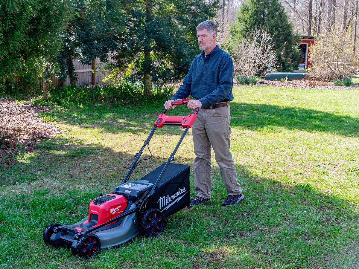 A man operating Milwaukee battery-powered lawn mower on a sunny day.