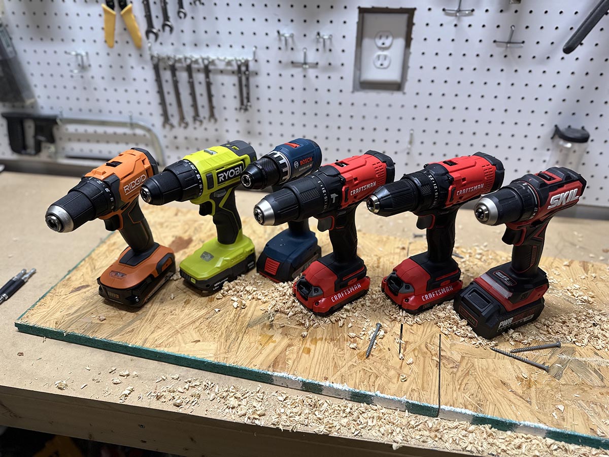 A group of the Best Cordless Drills Under $100 on a workbench before testing.