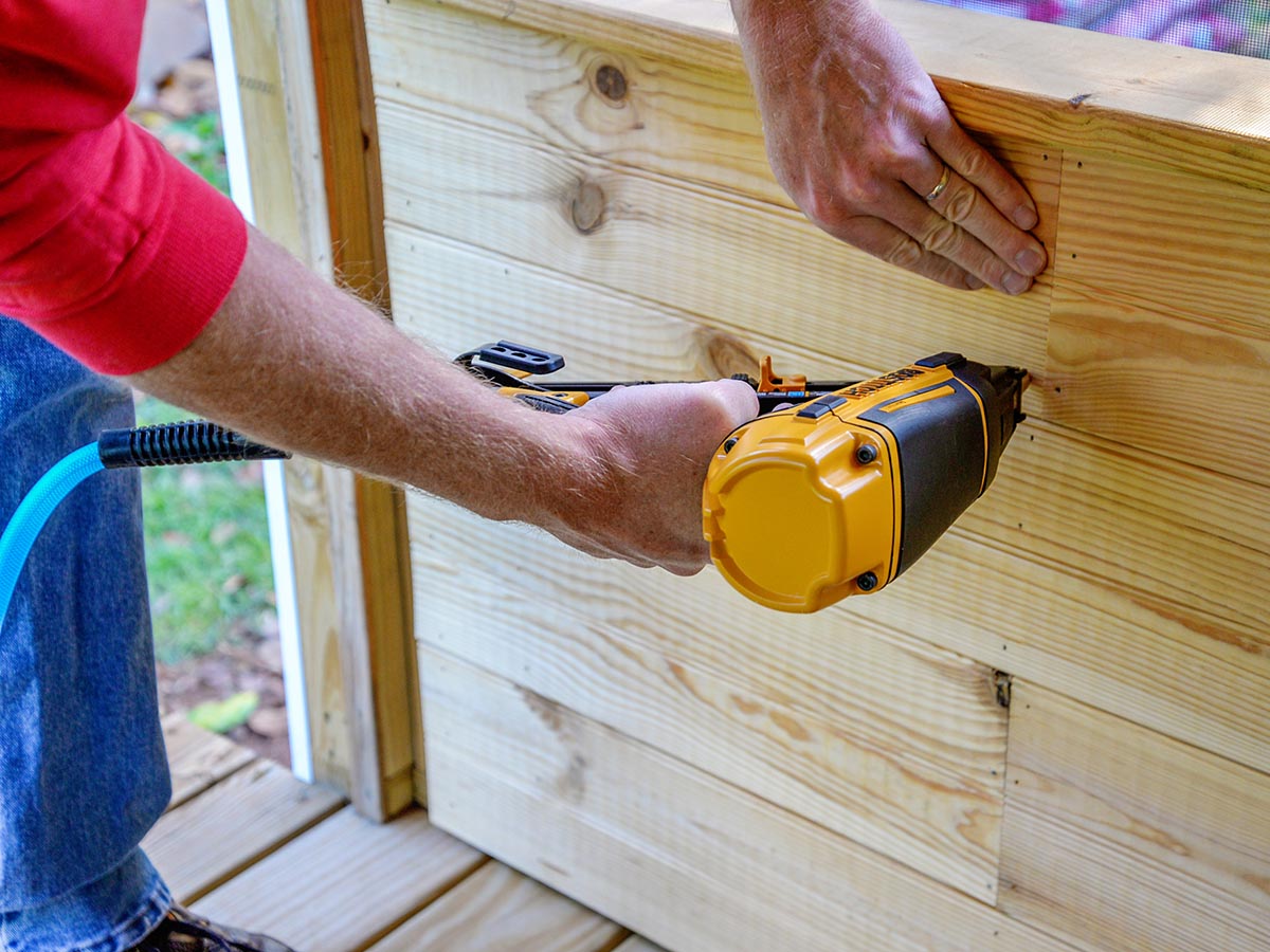 A person using the DeWalt 20V MAX XR 16 GA Cordless Angled Finish Nailer to attach paneling in a porch.